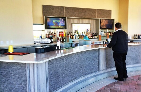 A bar area with a curved counter, multiple bottles, and a television screen.