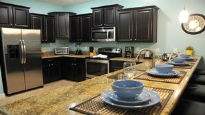 A modern kitchen with dark cabinetry, stainless steel appliances, and a granite countertop. - Ov3992 - Champions Gate Resort - 8 Bed 5 Baths Villa (Davenport)