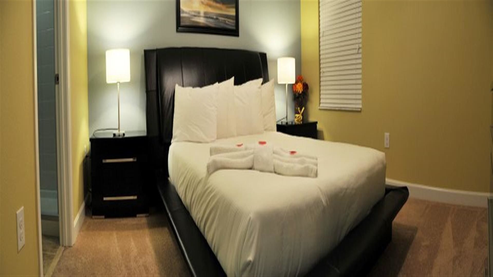 A neatly made bed with white linens and towels, two bedside lamps, and a framed picture on the wall.