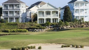 A coastal property with multiple multi-story houses, a well-maintained lawn, and a sandy beach area.