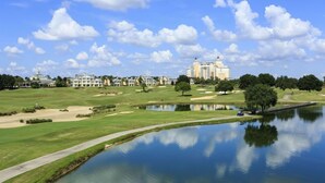 A golf course with a pond, a walking path, and a large hotel in the background.