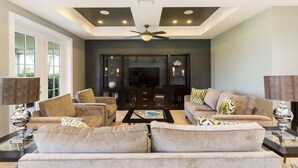 A modern living room with a large flat-screen TV, dark wood cabinets, and beige sofas.