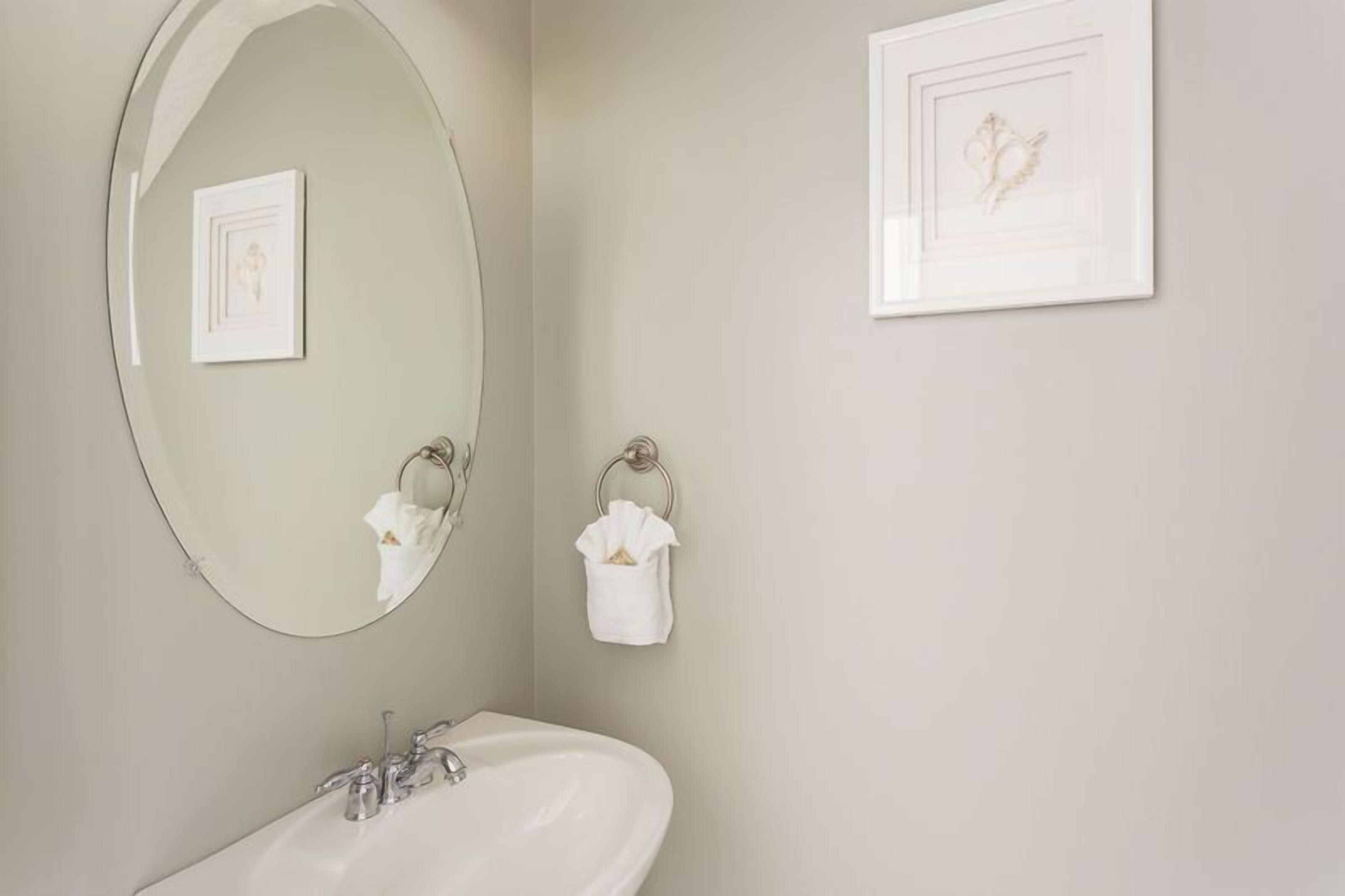 Een badkamer met een ronde spiegel, een wastafel en twee handdoekrekken met witte handdoeken.