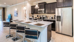 Una cocina moderna con armarios oscuros, electrodomésticos de acero inoxidable y una isla central con taburetes de bar.