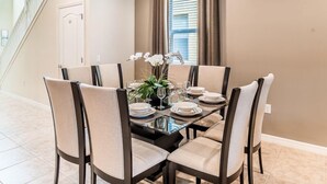 Un comedor con una mesa de vidrio, sillas color beige y un jarrón de flores blancas.