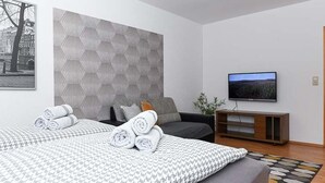 Moderni hotellihuone, jossa on suuri sänky, televisio ja geometrisesti kuvioitu sängynpääty.