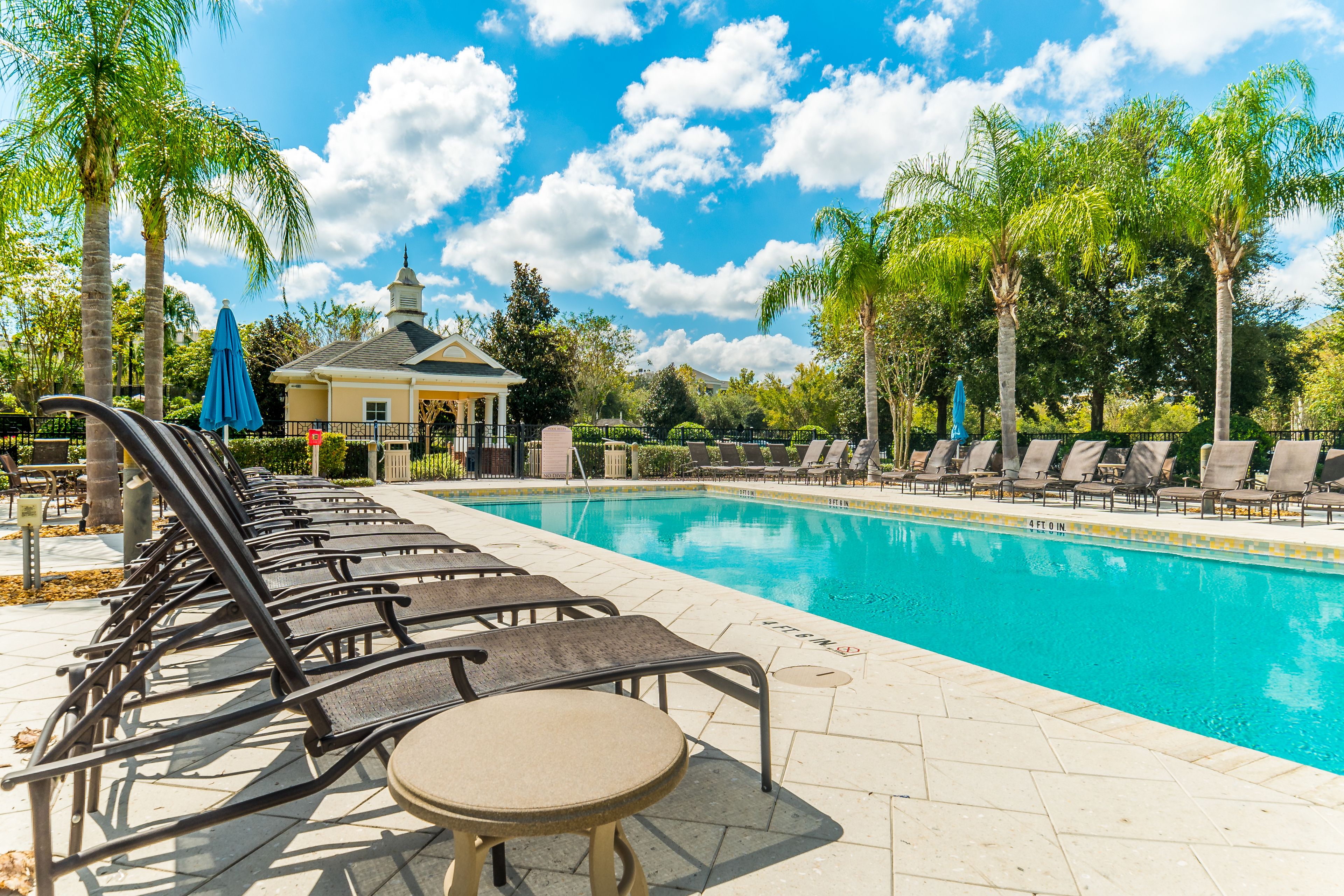 A poolside area with lounge chairs and a small table, surrounded by palm trees and a building with a dome roof.