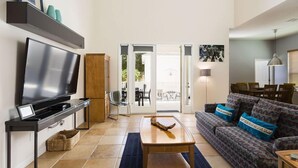 Ein Wohnzimmer mit Flachbildfernseher, Couchtisch aus Holz, gestreiftem Sofa und einem Essbereich mit Stühlen und Tisch.
