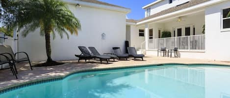 A swimming pool with lounge chairs, a palm tree, and a building with a balcony.