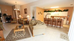 A living room with a sofa, coffee table, and chairs, a kitchen with a dining area, and a small office space with a desk and chair.