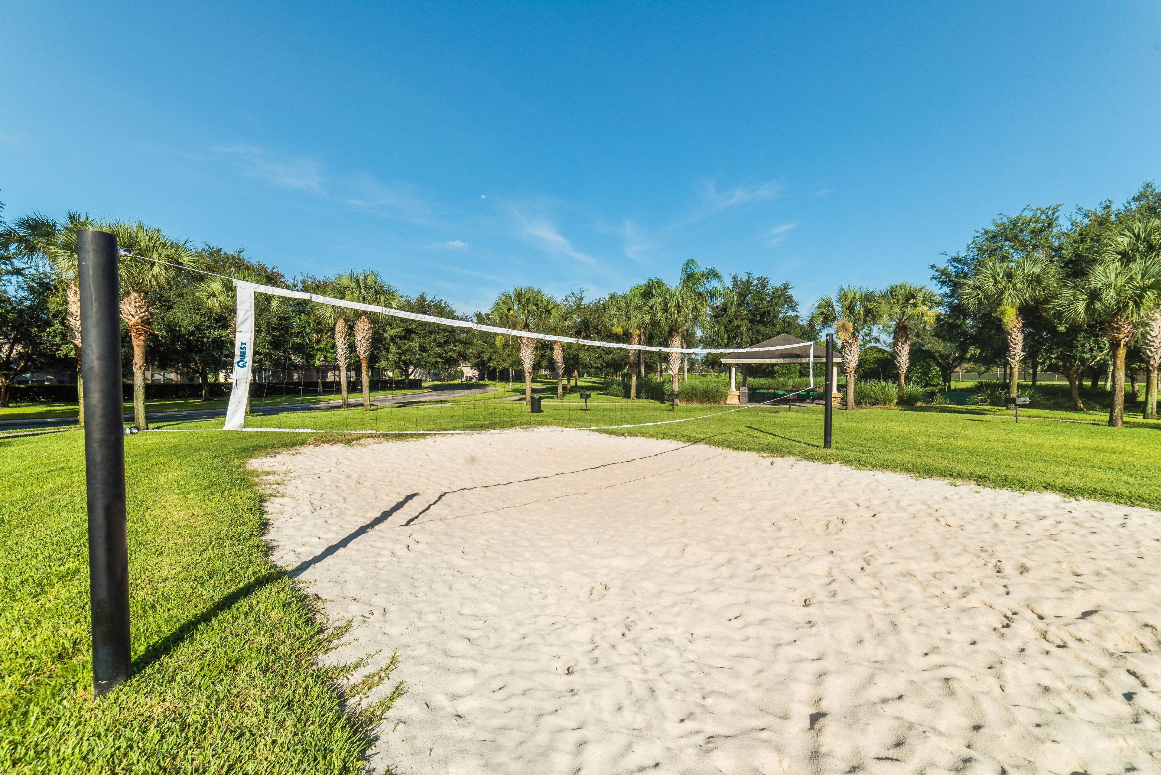A volleyball court with a net, surrounded by sand and greenery.
