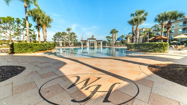 A pool area with palm trees, a gazebo, and a building with balconies.