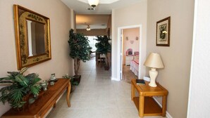 A hallway with a wooden bench, a mirror, a lamp, and potted plants.
