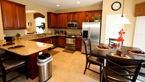 A modern kitchen with granite countertops, stainless steel appliances, wooden cabinets, and a dining area with a table and chairs.