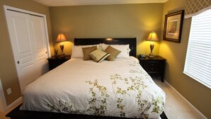 A neatly made bed with a floral bedspread, two bedside lamps, a framed picture on the wall, and a window with blinds.