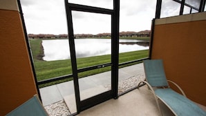 Ein Zimmer mit einem großen Fenster mit Blick auf einen See und entfernte Gebäude. Zwei blaue Sitzgelegenheiten und ein kleiner Tisch sind vorhanden.