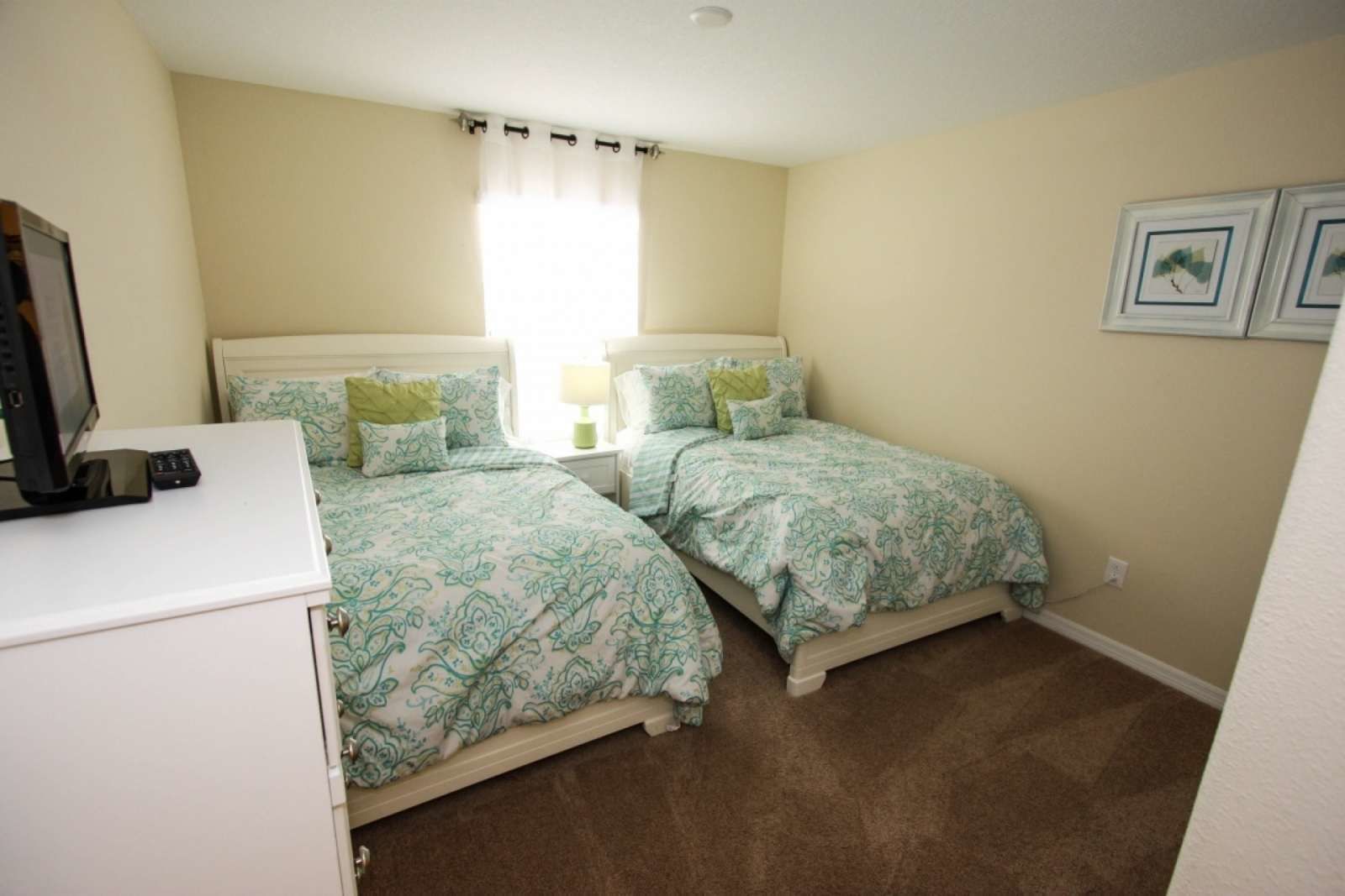 A bedroom with two beds, a desk, and a television.