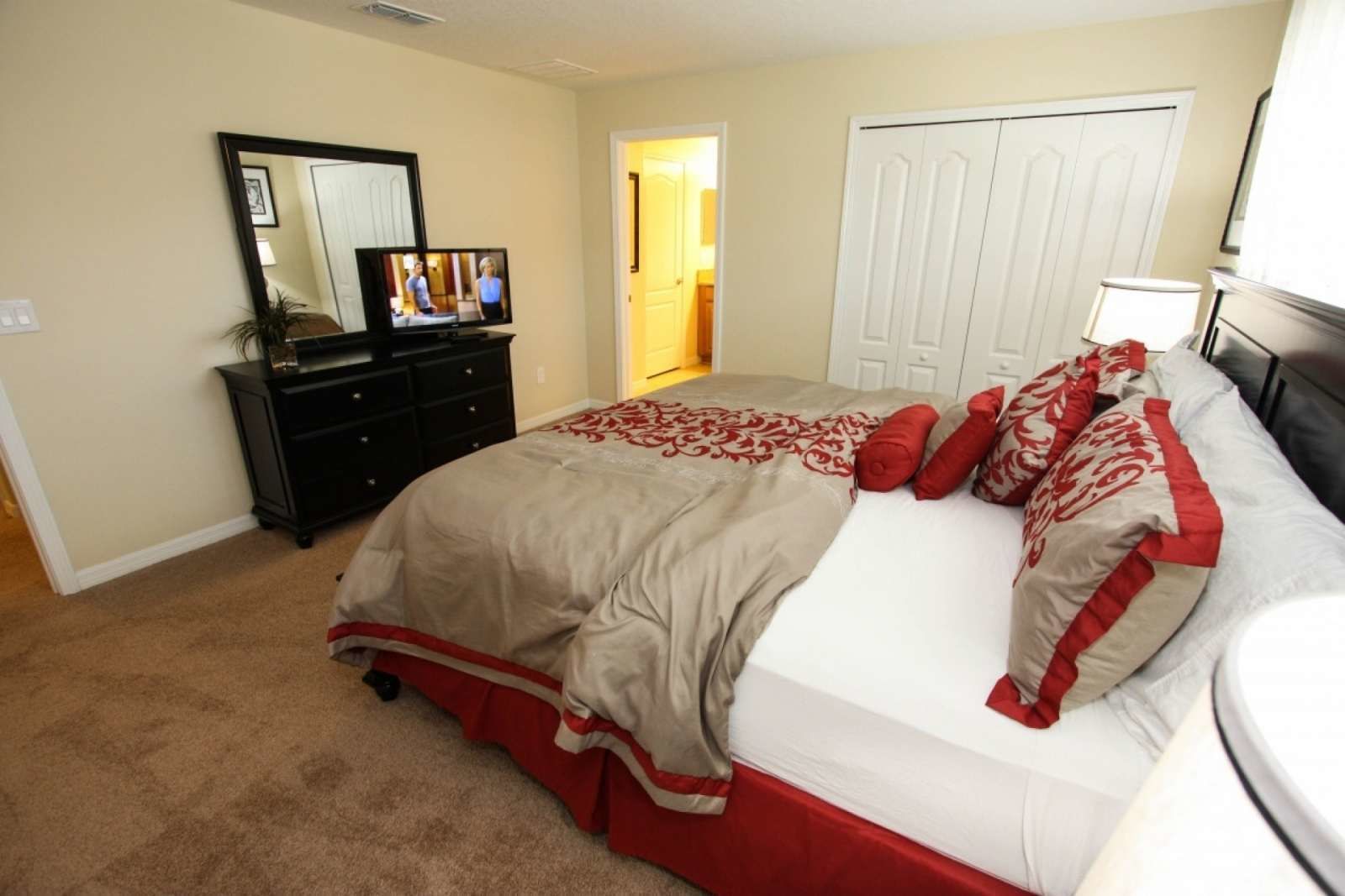 A bedroom with a bed, a dresser, a mirror, and a television.