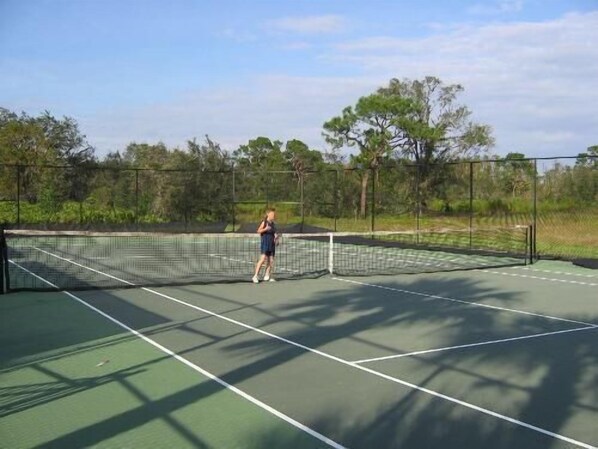 Una cancha de tenis con red, rodeada de árboles y una valla.