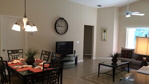 A dining area with a table set for four, a television, and a clock on the wall.