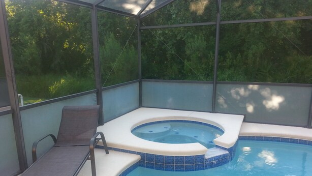 A hot tub with a tiled edge, a lounge chair, and a glass enclosure.