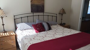 A bedroom with a bed, two bedside tables, a nightstand, a lamp, and a painting on the wall.