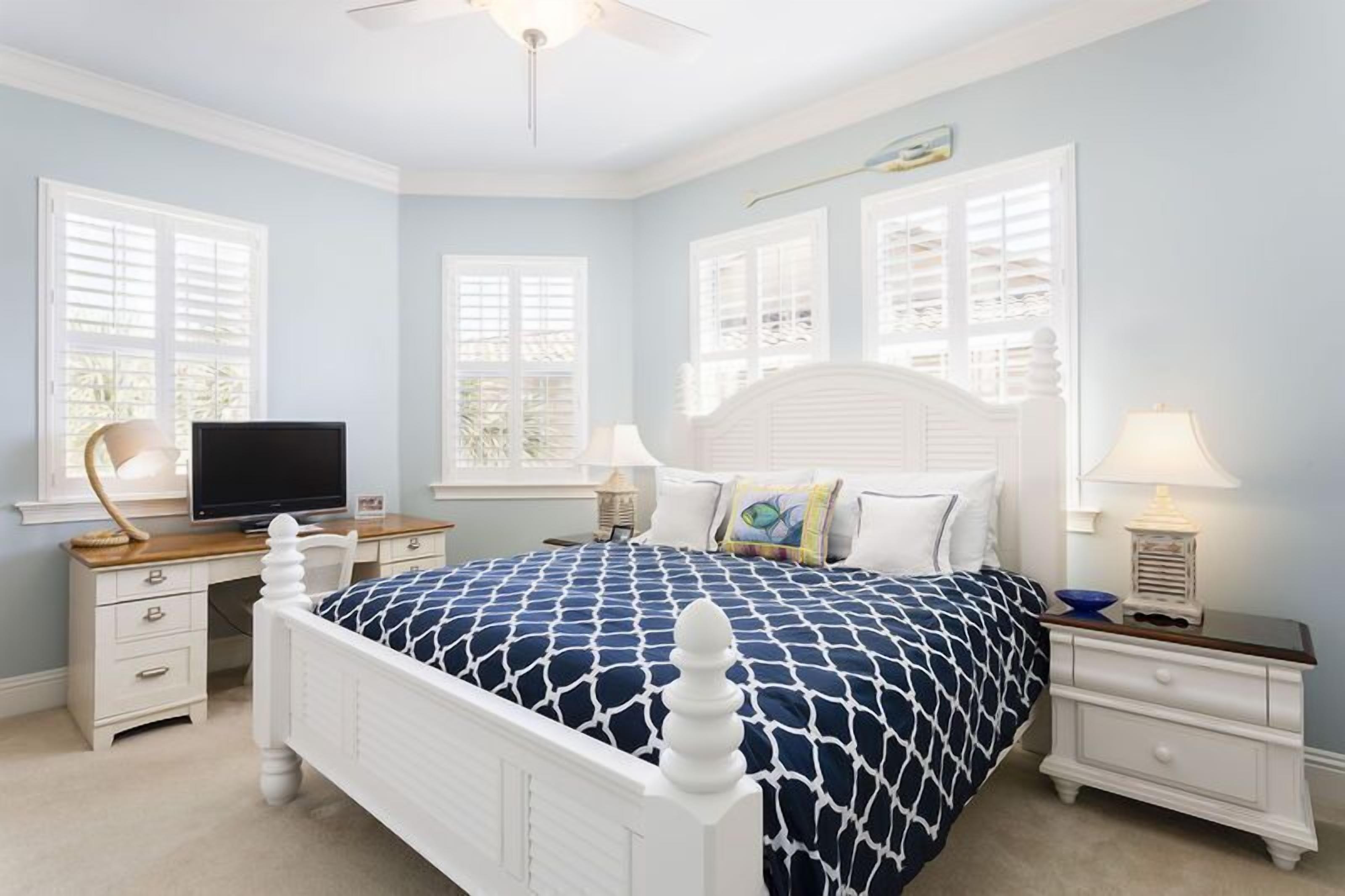 A bedroom with a bed, two bedside tables, a desk, a chair, and a television.
