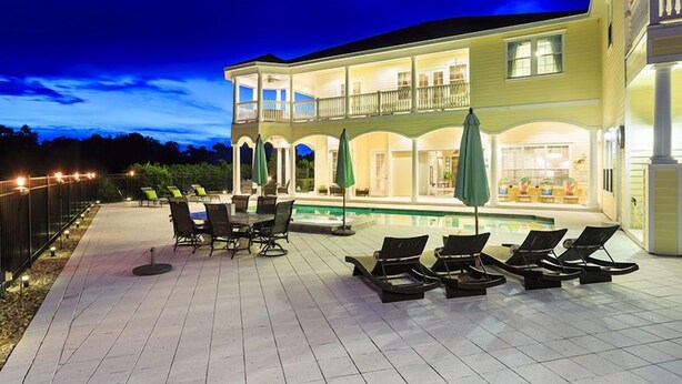 Una casa de dos pisos con piscina, mobiliario exterior y un patio bien iluminado.