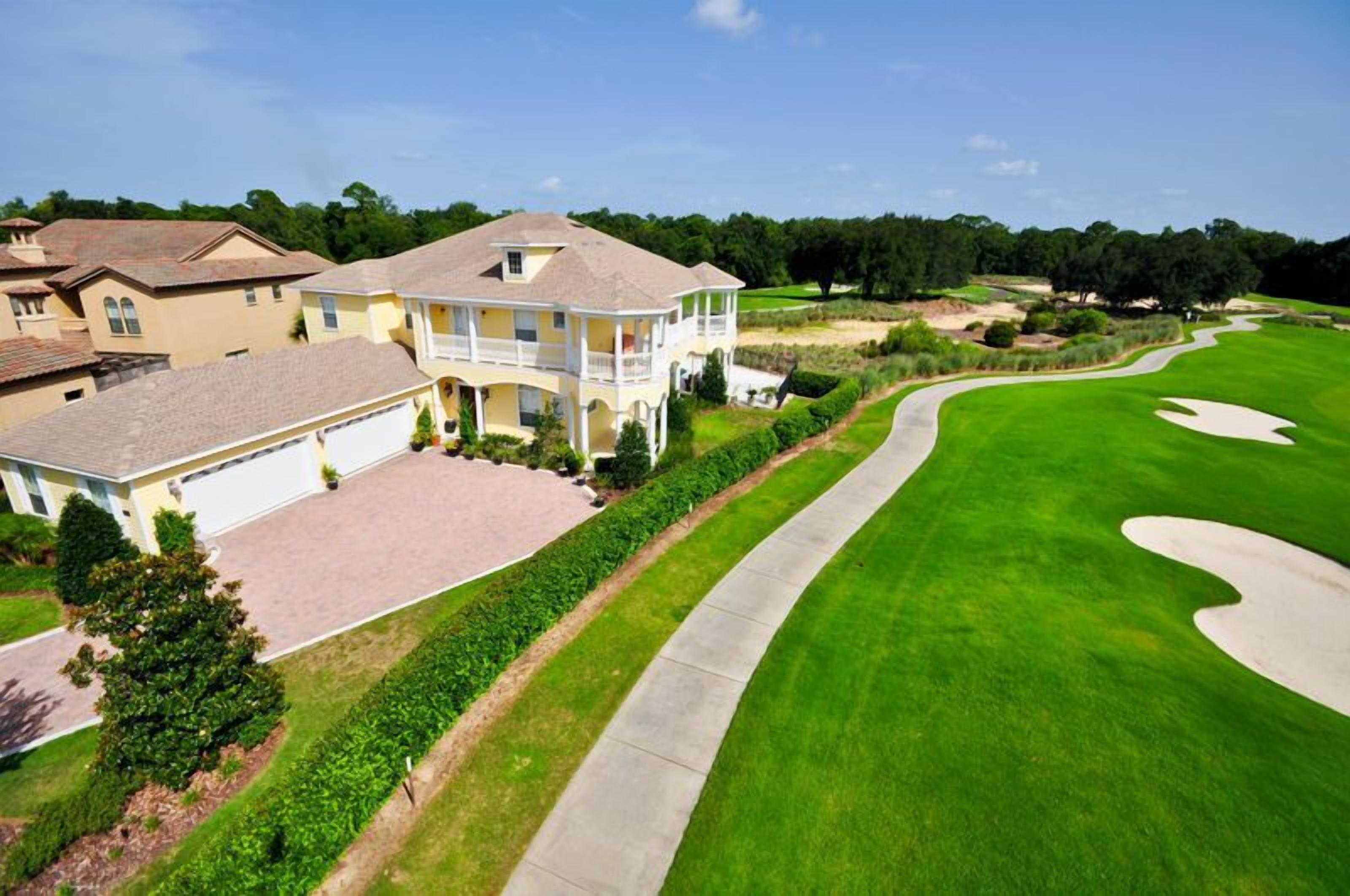 A golf course with a well-maintained green, a winding path, and a large house with a driveway and garage.