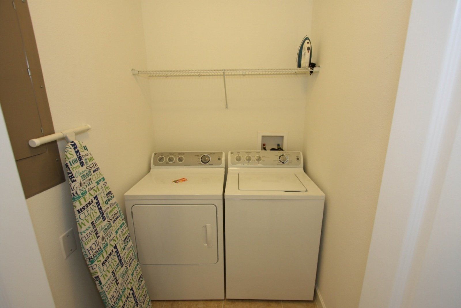 A laundry room with two white washers and dryers, a metal shelf above the dryers, and a towel rack with a patterned towel.