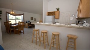 Een keuken met een eettafel, barstoelen, een koelkast en houten kastjes.