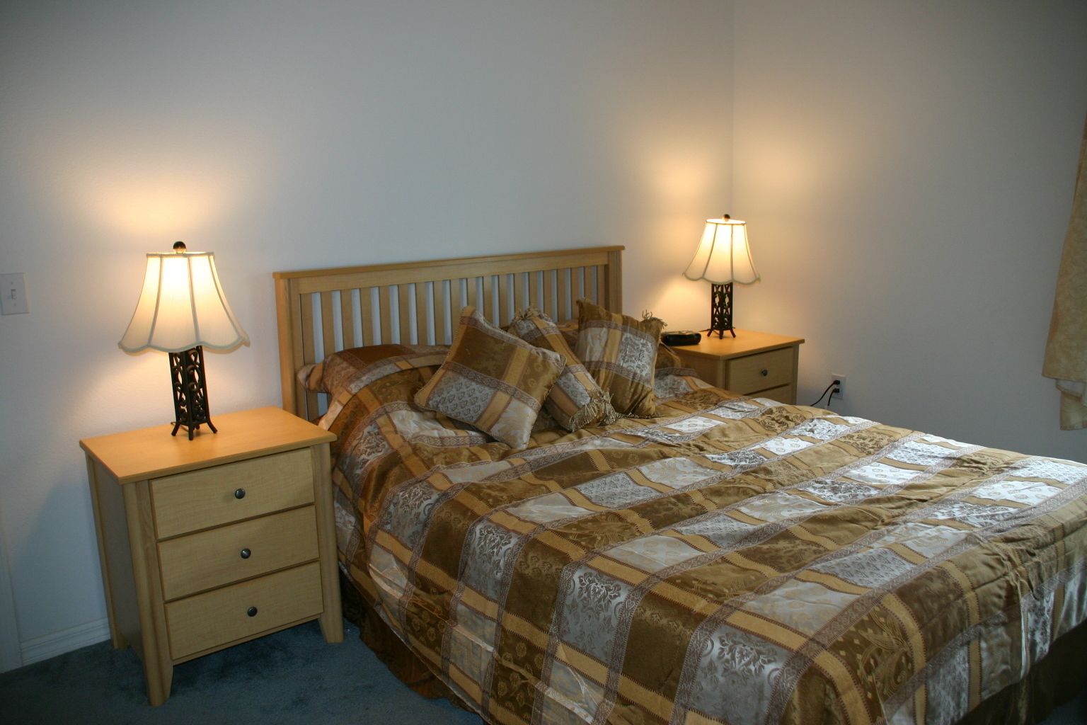 Una cama bien hecha con un edredón estampado, dos mesitas de noche con lámparas y un cabecero de madera.