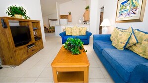 Een woonkamer met een houten tv-meubel, een blauwe bank en een houten salontafel.