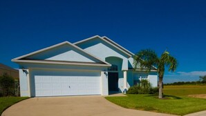 Een gelijkvloers huis met een witte garage, een voordeur en een kleine voortuin met een palmboom.