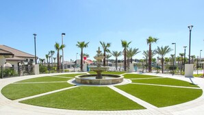 Ein angelegter Garten mit einer zentralen Fontäne, umgeben von Rasenflächen und Palmen.