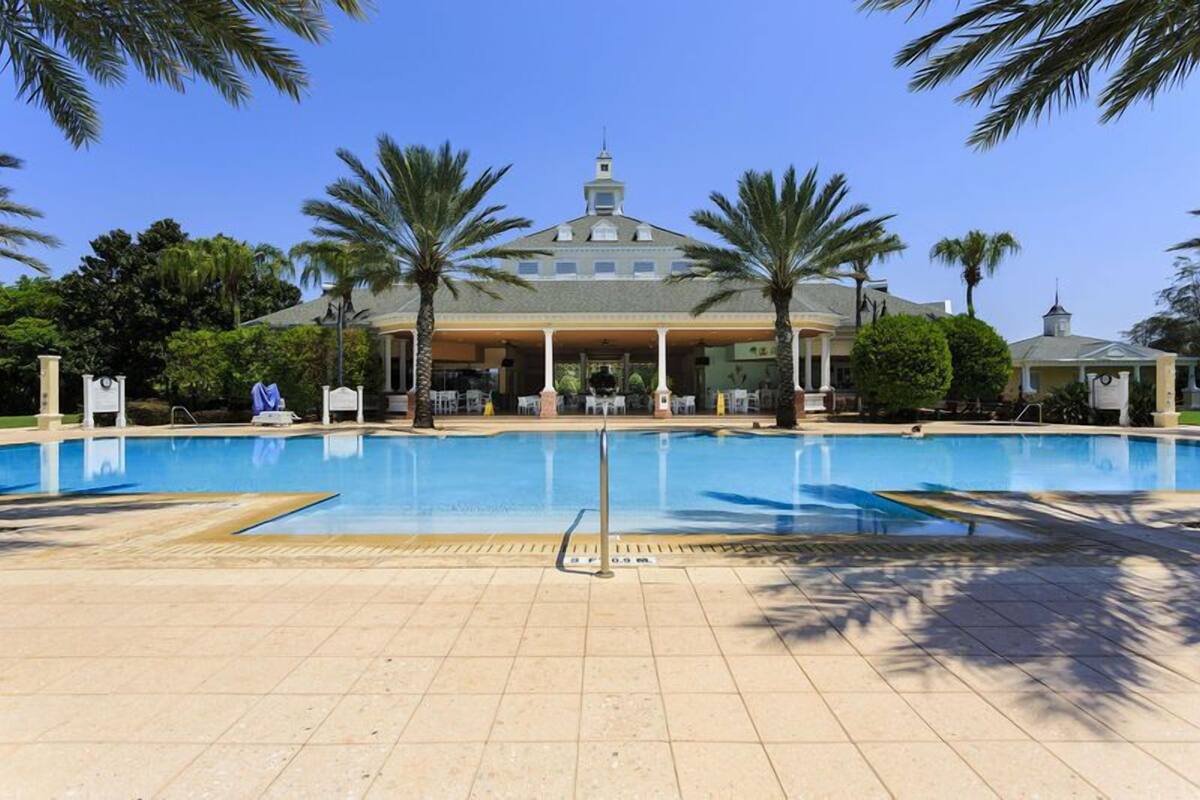 Une piscine avec une terrasse carrelée, des palmiers et, au fond, un bâtiment surmonté d’un dôme.