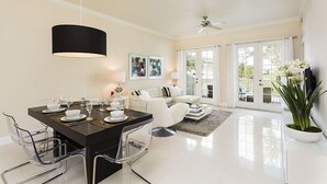 Un salon moderne avec un coin repas, comprenant une table à manger noire pour quatre personnes, des canapés blancs et une grande fenêtre donnant sur l’extérieur.