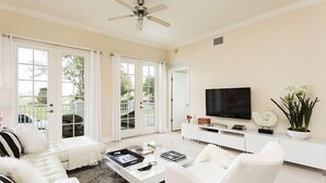 Un salon moderne avec un canapé blanc, une table basse, un téléviseur et une grande fenêtre avec des rideaux.
