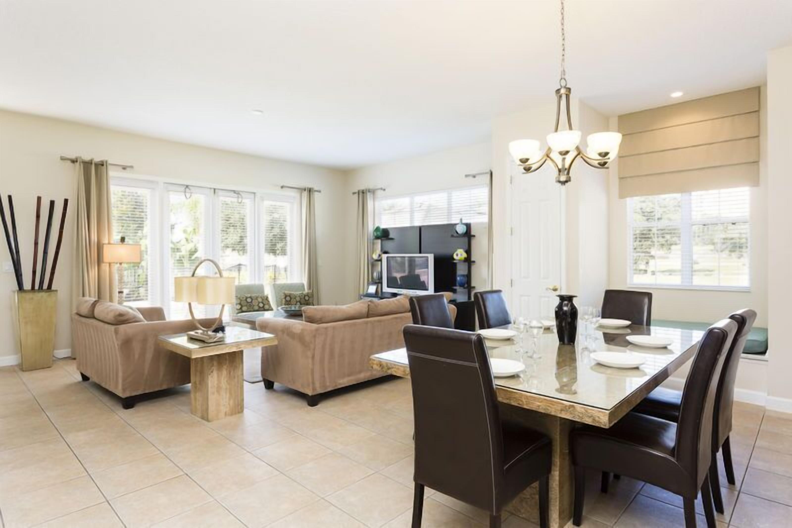 A spacious living room with a dining area, beige sofas, a wooden coffee table, and a large TV.