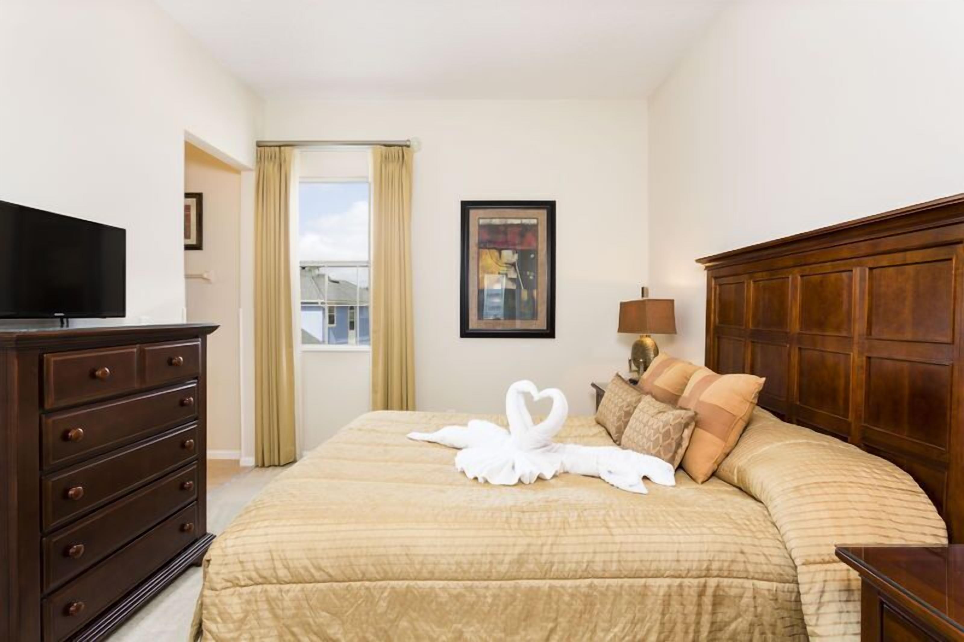 Quarto de hotel com uma cama grande, cômoda, televisão e janela com cortinas.