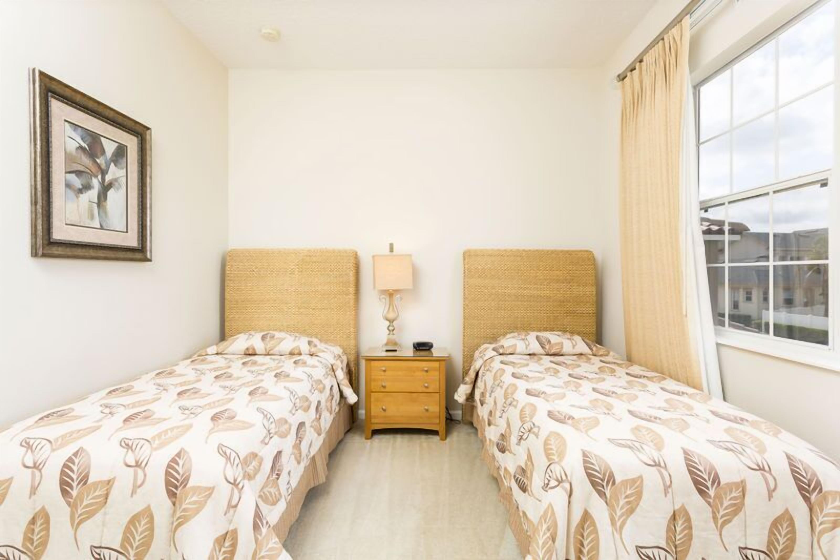 Een hotelkamer met twee eenpersoonsbedden, een klein nachtkastje met een lamp, een lijst met een foto aan de muur en een raam met gordijnen.