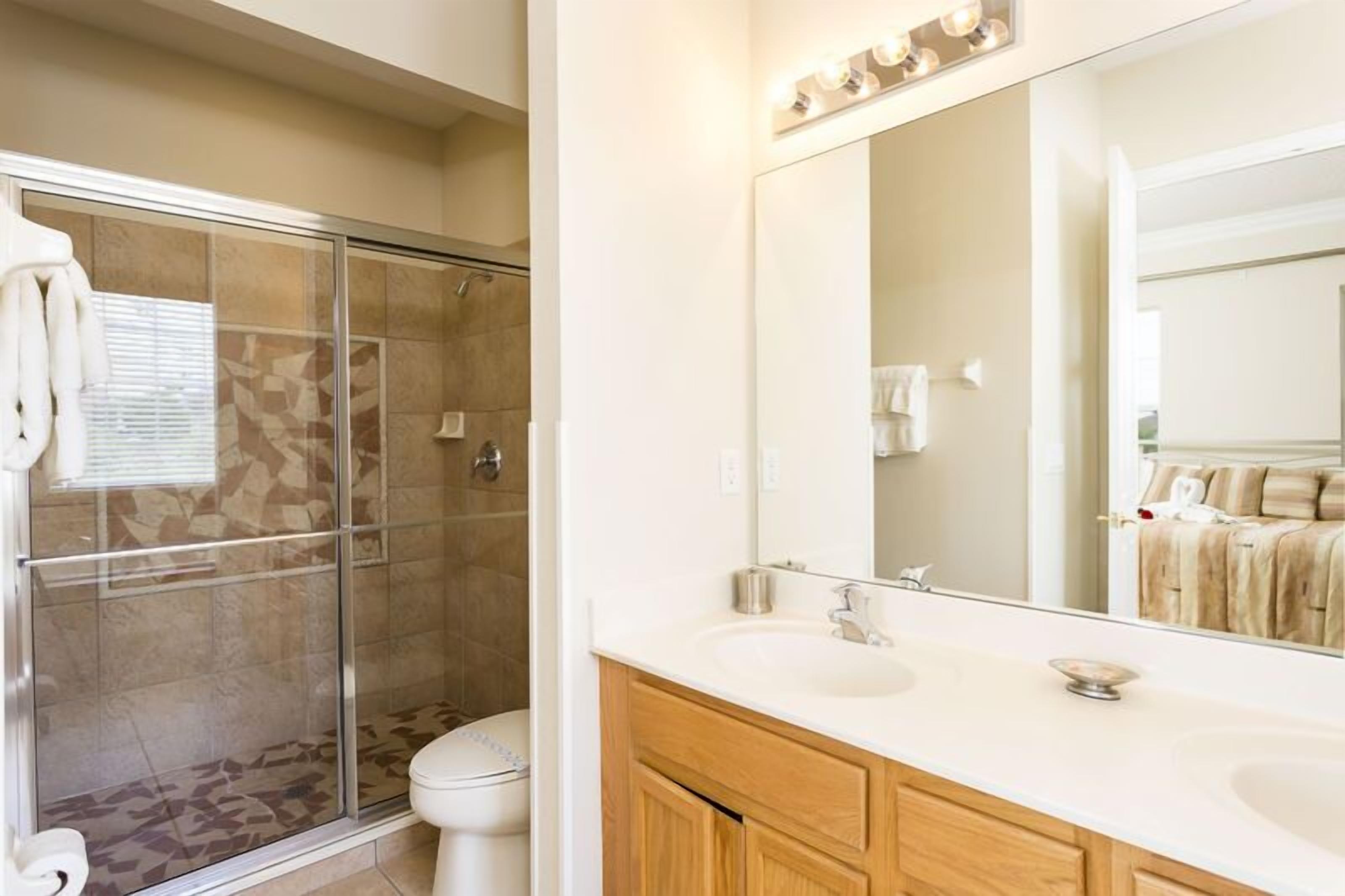 A modern bathroom with a glass-enclosed shower, a large mirror, and a dual sink vanity.
