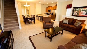 A living room with a brown sofa, a coffee table, and a dining area with a table and chairs. - Ov4254 - Paradise Palms - 5 Bed 4 Baths Townhome (Kissimmee)
