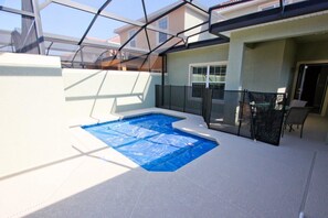 Una piscina interior con cerramiento de cristal, rodeada por una zona de patio con sillas y una mesa.