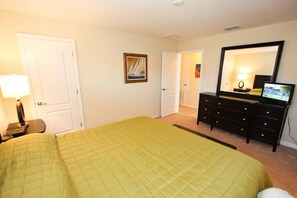 Un dormitorio con cama, cómoda, televisor y puerta que da a otra habitación.