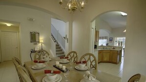 A dining area with a large table set for six, surrounded by wooden chairs. A staircase is visible in the background leading to another level. - Ov2625 - Emerald Island - 5 Bed 4 Baths Villa (Kissimmee)