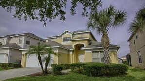 A two-story residential building with a yellow facade, a garage, and a well-maintained lawn with palm trees. - Ov2625 - Emerald Island - 5 Bed 4 Baths Villa (Kissimmee)