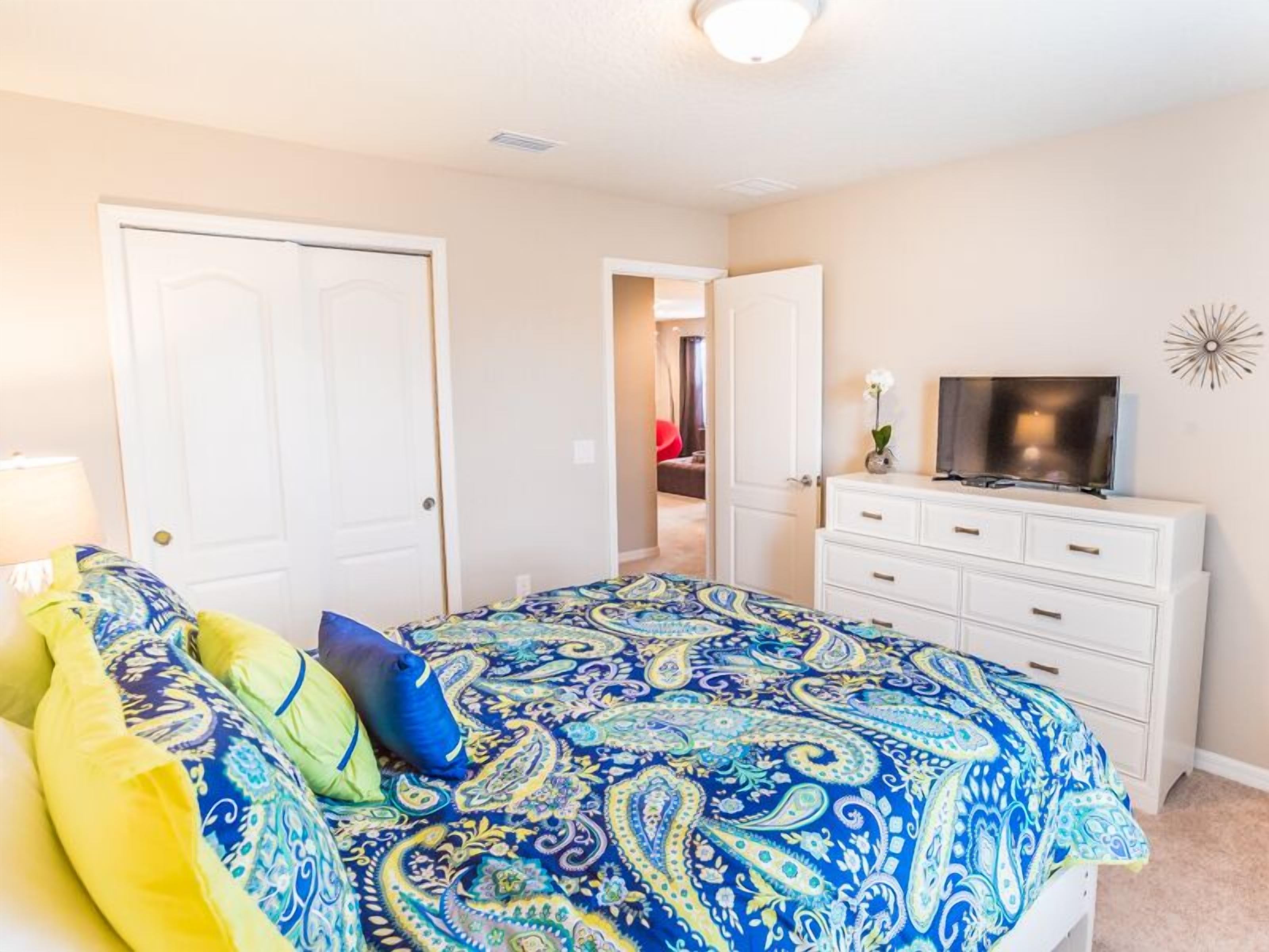 A bedroom with a bed, a dresser, a television, and a door.