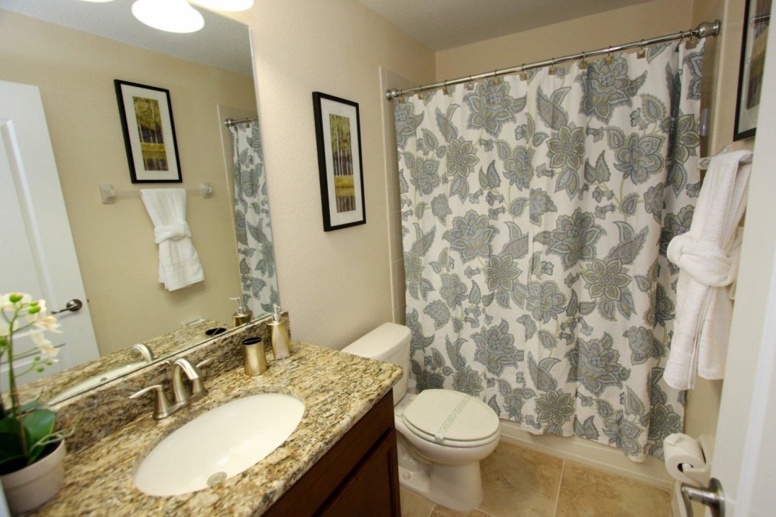 A bathroom with a granite sink, a toilet, and a shower curtain with a floral pattern.