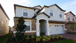 A two-story residential building with a stone facade, a garage, and a landscaped front yard.